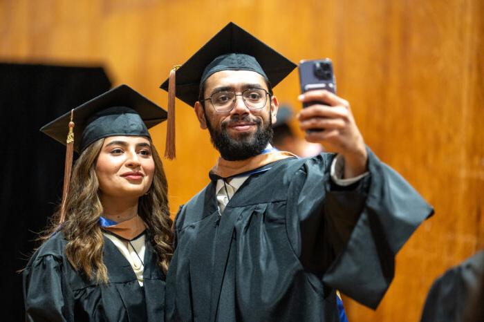 A pair of college graduates take a selfie in their caps and gowns.